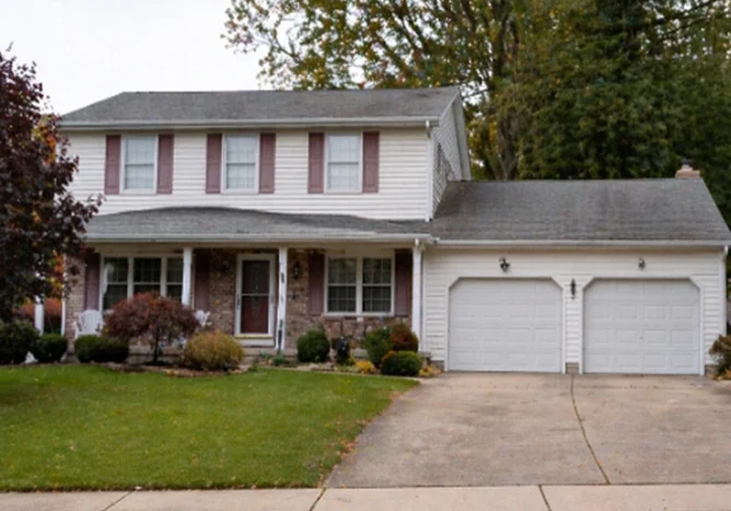 sell-house-divorse-fast-img A quiet, well-maintained NJ suburban home at midday — colonial or split-level from the 1980s or 1990s, established trees, two-car driveway. Looks lived-in and solid. No people. Overcast NJ sky. The mood is still and bittersweet — a home at the end of a chapter. Realistic photography style.